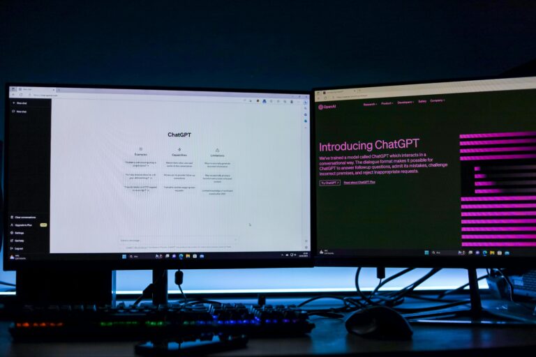 Dwa monitory na biurku z interfejsem chatbota, z podświetlaną klawiaturą i myszką z przodu