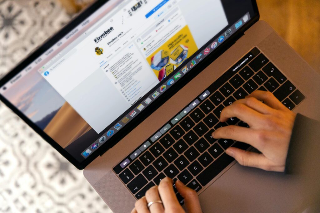 Dłonie na klawiaturze laptopa widziane z góry, na ekranie otwarta strona internetowa