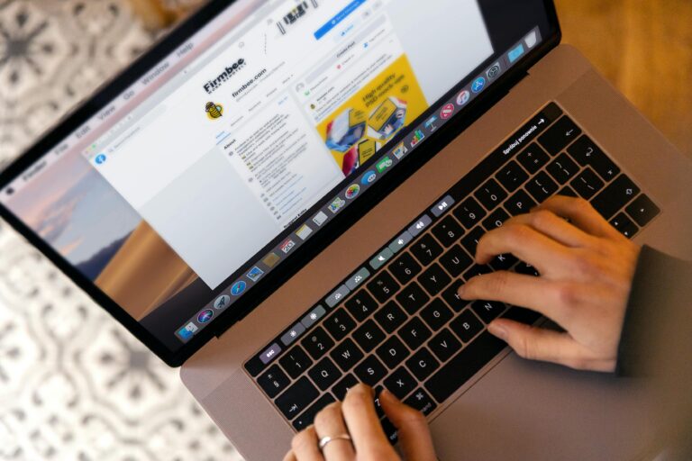 Dłonie na klawiaturze laptopa widziane z góry, na ekranie otwarta strona internetowa