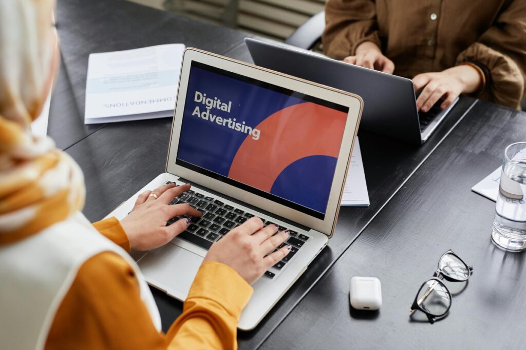 Kobieta w chuście pisze na laptopie ze slajdem Digital Advertising, przy stole siedzi koleżanka