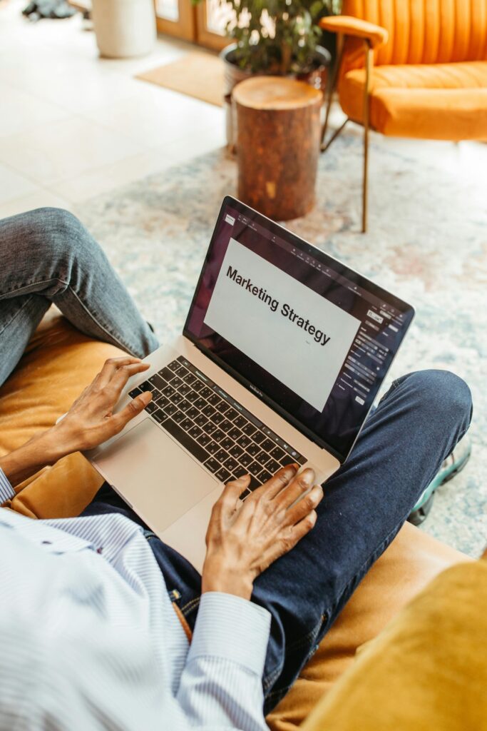 Osoba na sofie pisze na laptopie położonym na kolanach, na ekranie slajd Marketing Strategy