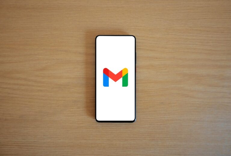 Smartfon leżący na drewnianym blacie z logo Gmail na białym ekranie