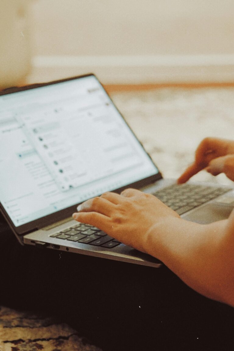 Zbliżenie na dłonie piszące na laptopie z rozmytą listą wiadomości na ekranie, w ciepłych barwach